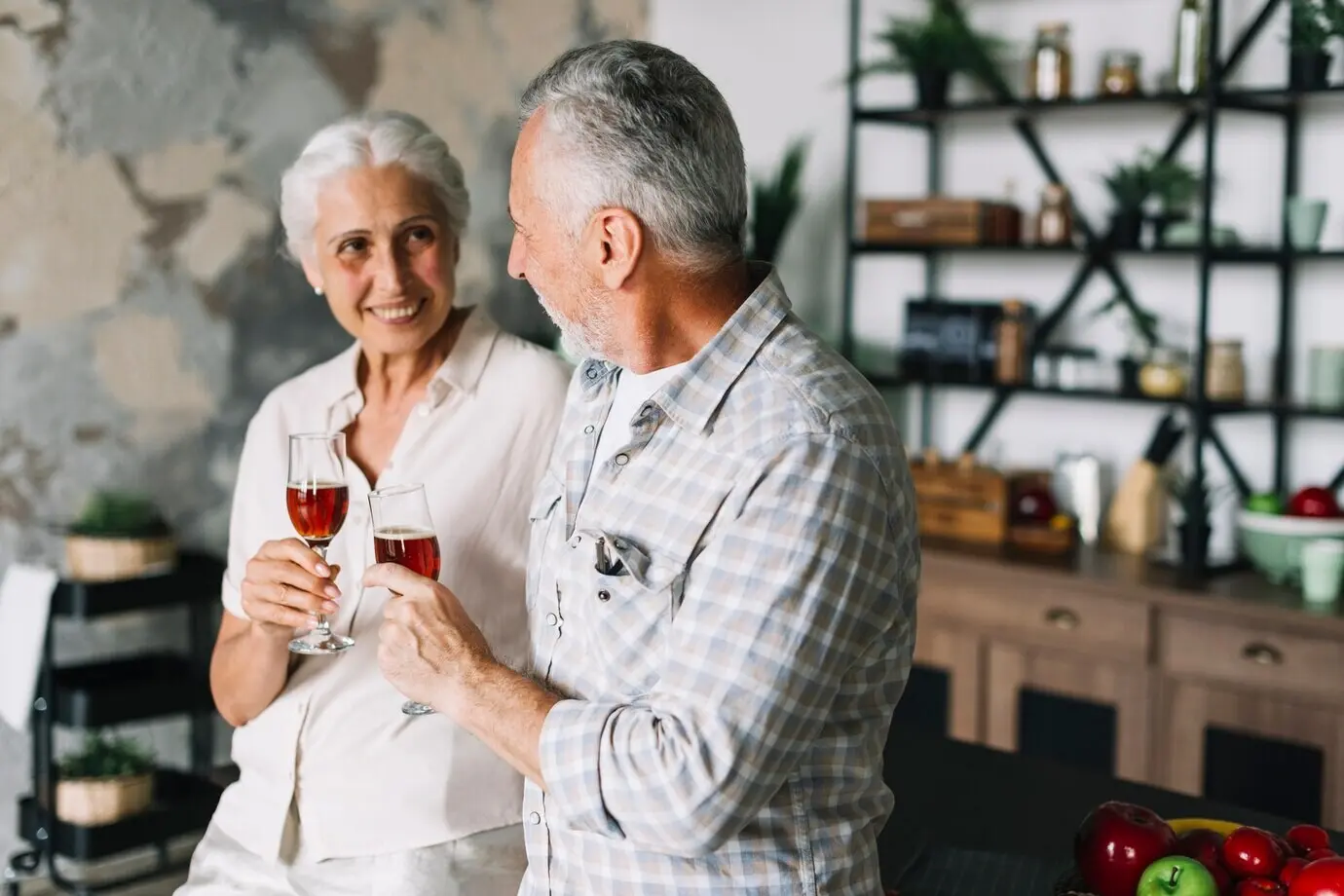 An elderly couple in the kitchen holding a glass of wine.